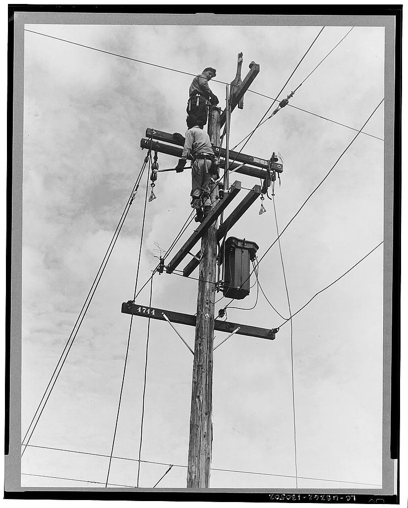 Linemen wiring a rural electrification power pole